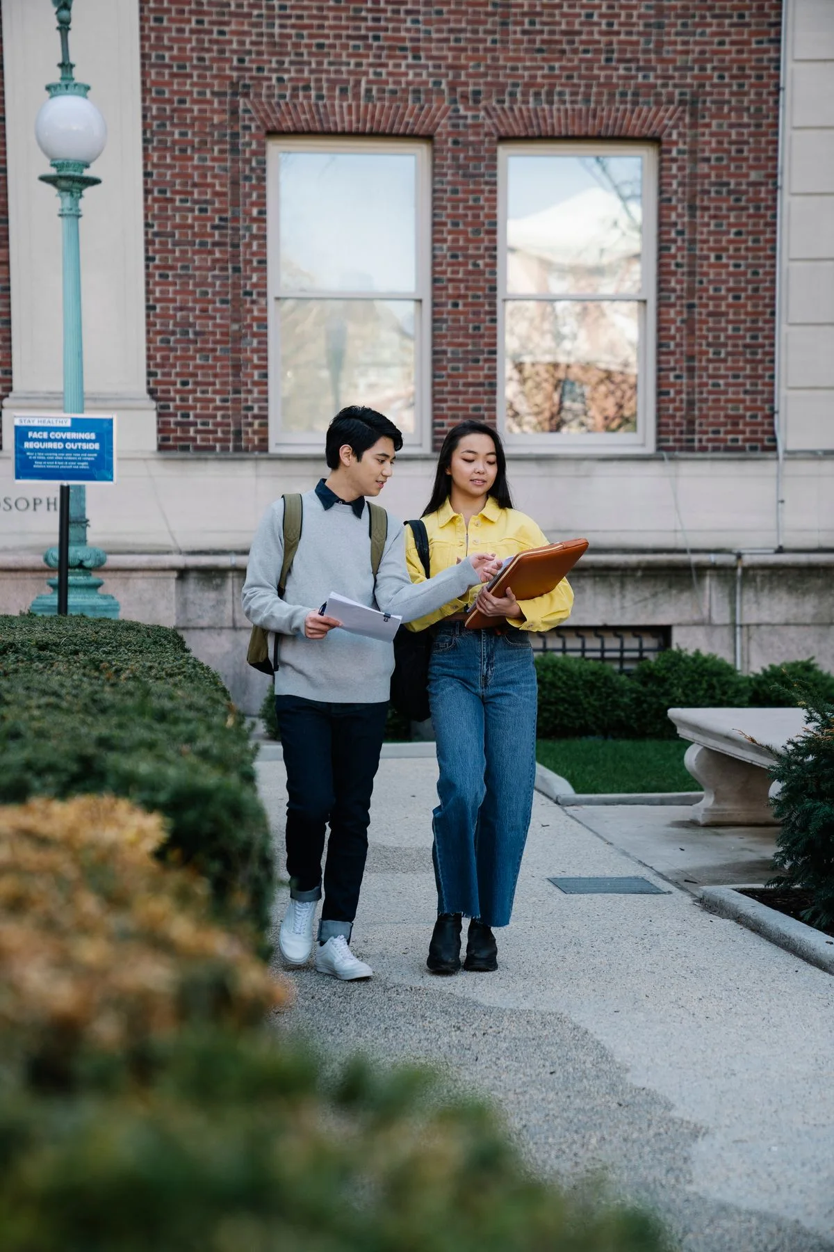 Two university students walking across campus while discussing their notes.