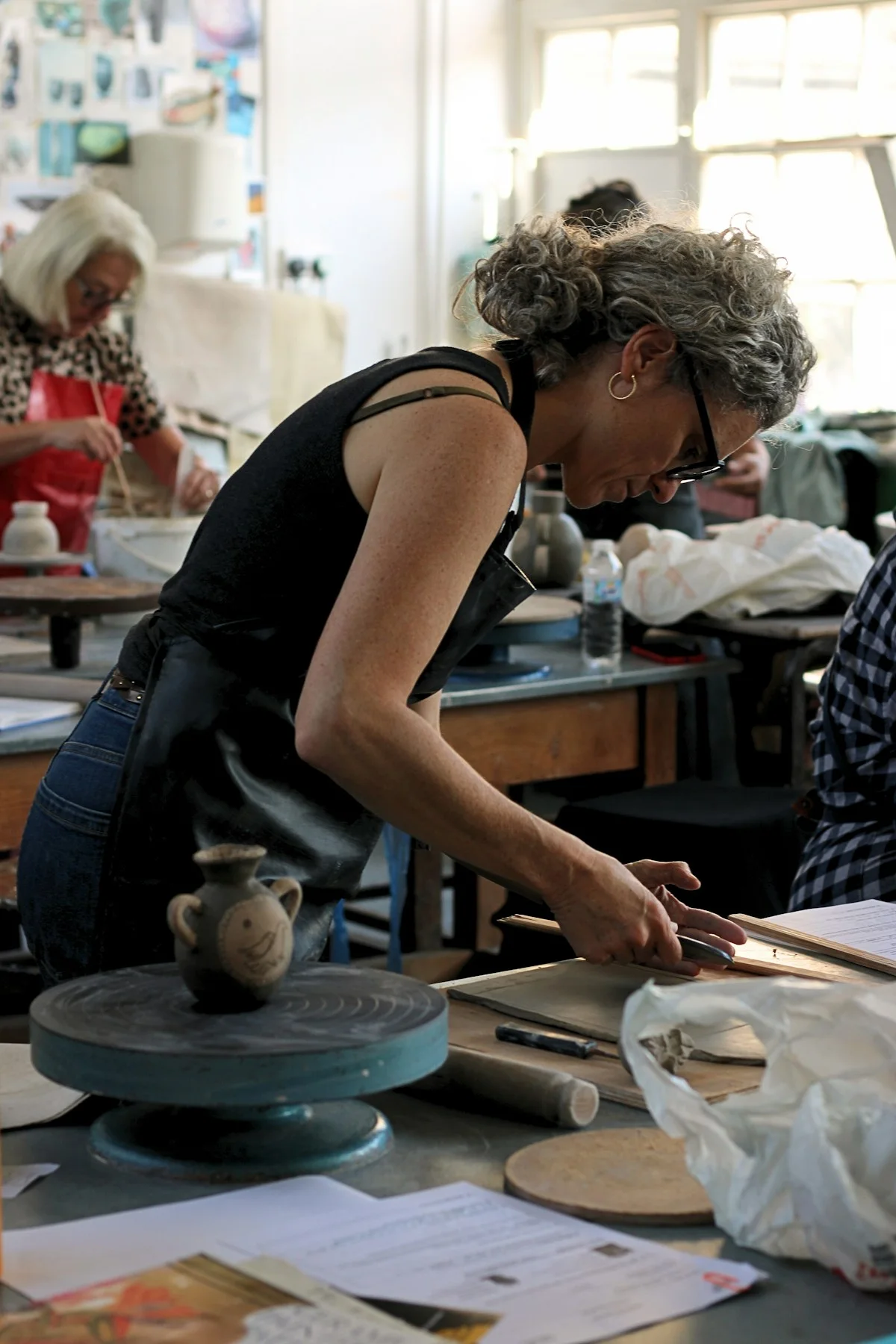 Woman shaping clay at a worktable in a daylight pottery studio.