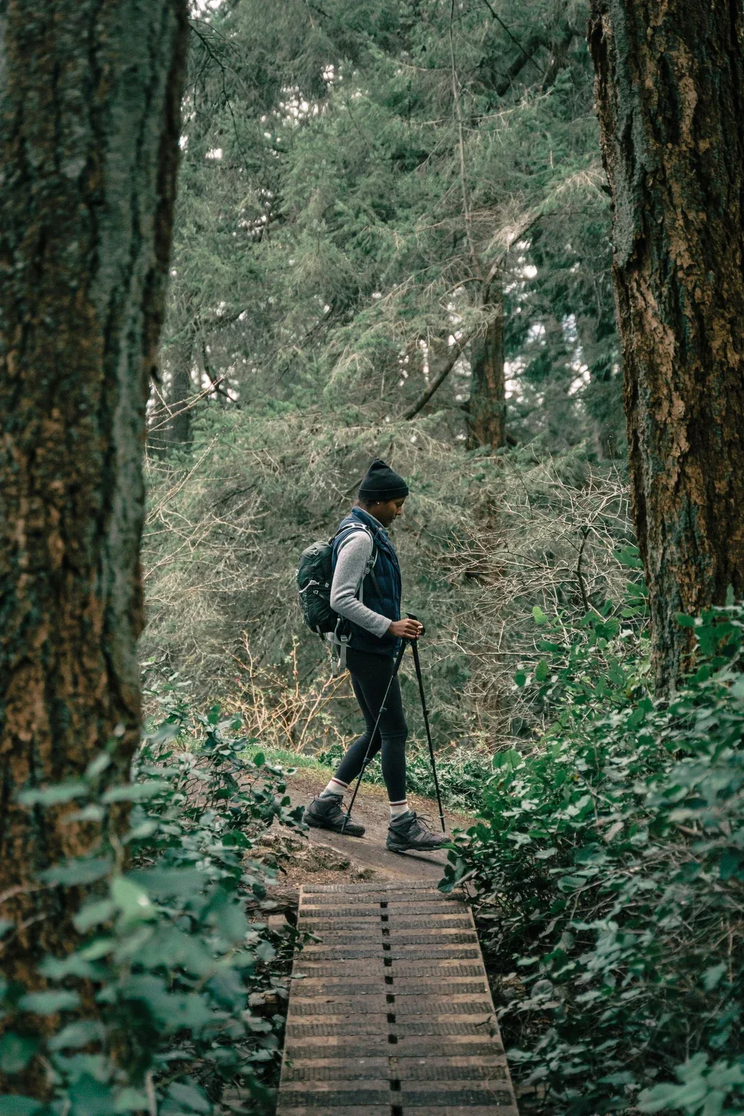 Woman with a backpack walking along a wooden path through a green forest.