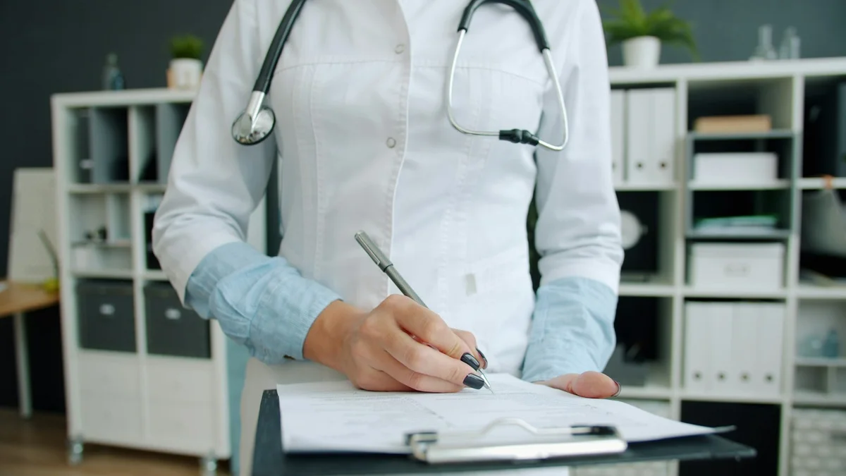 Close view of a healthcare professional writing on a clipboard.