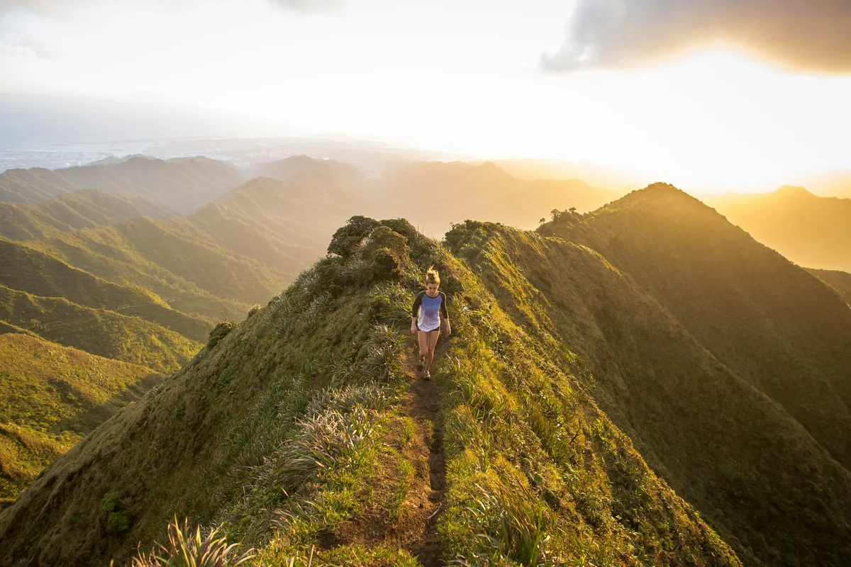 A woman walking along a sunlit mountain ridge