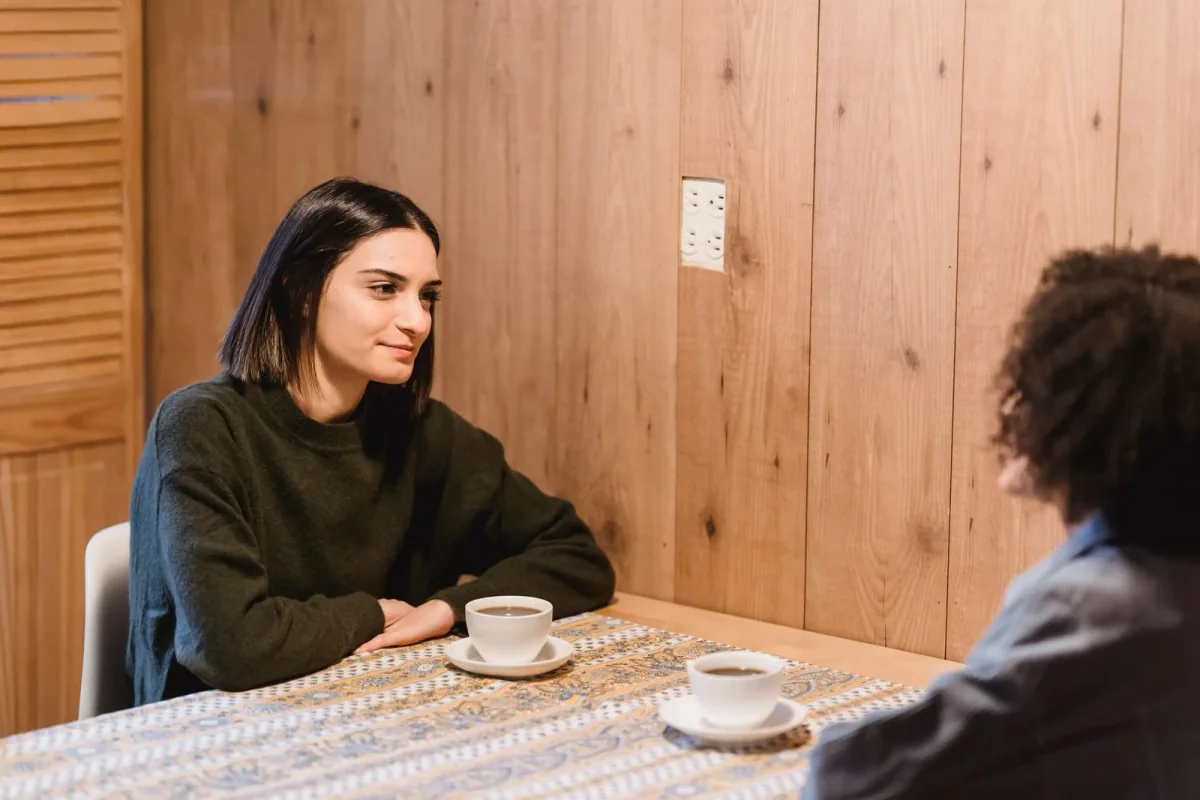 Two women talking over cups of coffee at a wooden cafe table.